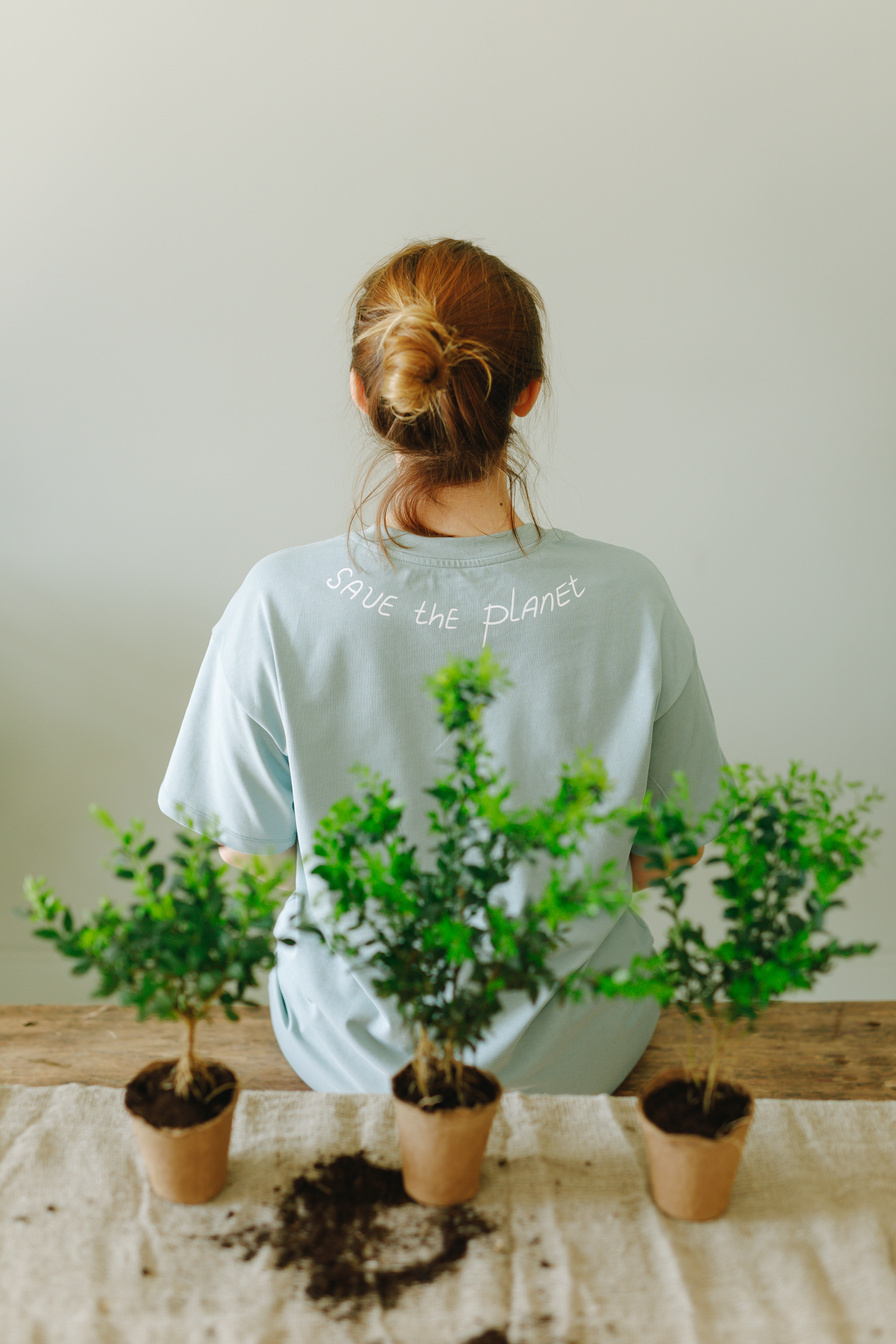 Woman Sitting Beside Potted Plants Wearing a Shirt with Save the Planet Text